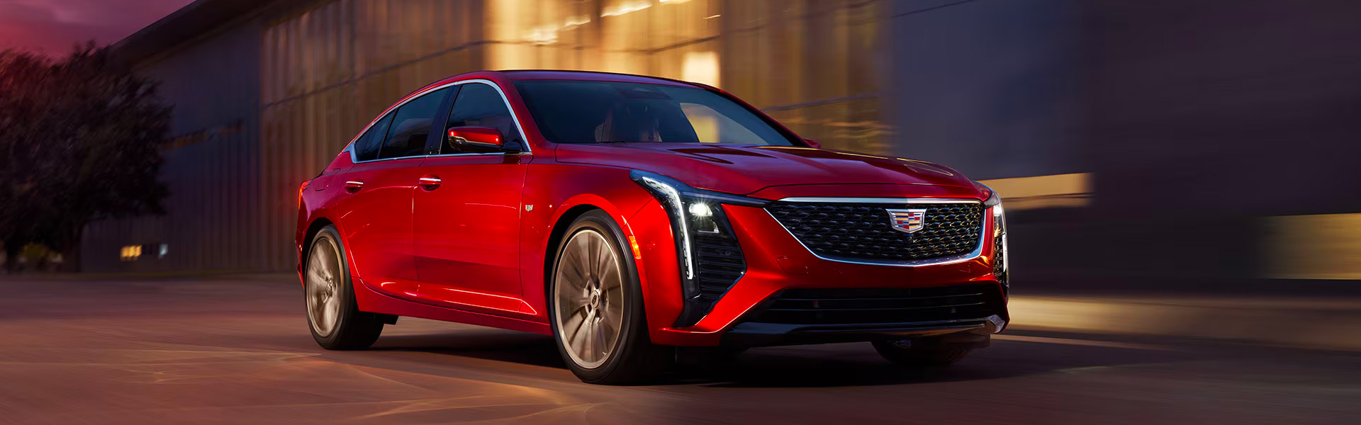 2025 Cadillac CT5 sedan in red driving through an urban setting at night.