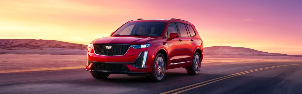 A red Cadillac XT6 SUV driving on a road at sunset.