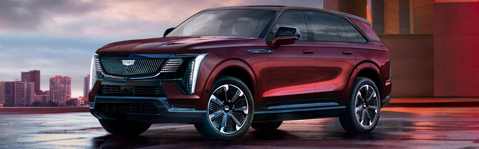 2026 Cadillac Escalade IQ in a rich maroon hue, showcased against an urban backdrop at sunset.