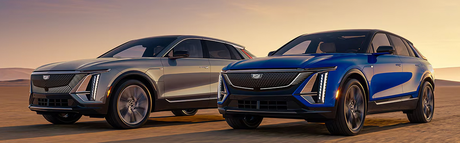 2026 Cadillac LYRIQ luxury SUVs in silver and blue parked on an open road at sunset.