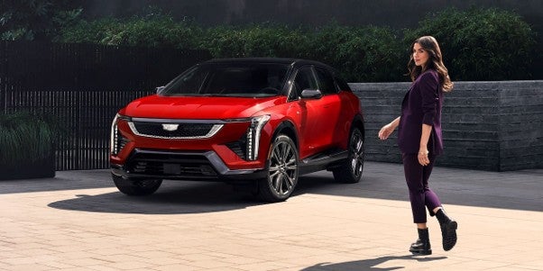2027 Cadillac OPTIQ electric SUV in red parked outdoors, showcasing its sleek design, distinctive vertical LED lighting, and modern luxury styling.