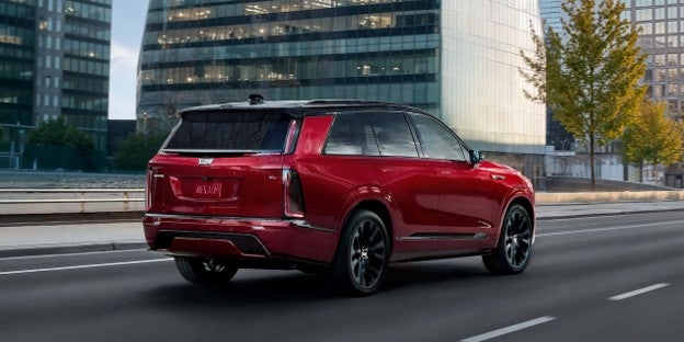 2027 Cadillac VISTIQ luxury electric SUV driving through a city, showcasing its sleek exterior design and distinctive vertical LED lighting.